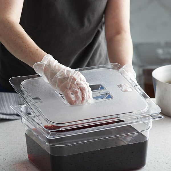 A person wearing gloves holding a Vigor clear plastic lid on a food container.