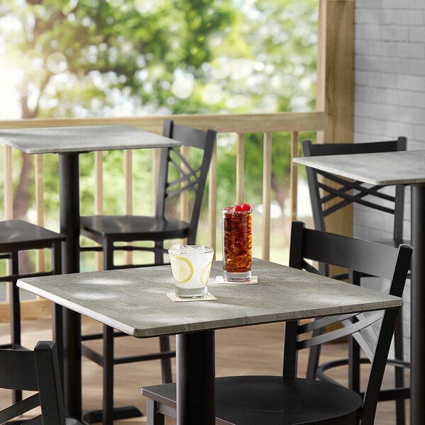 A Lancaster Table & Seating square table with textured Toscano finish, chairs, and a drink on it.