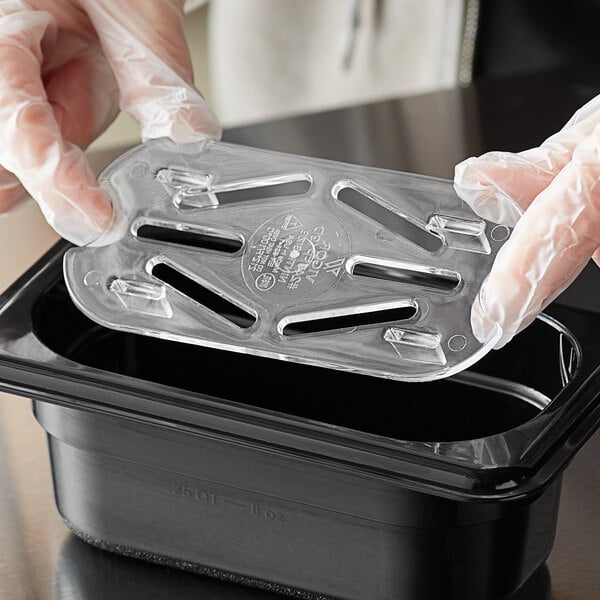 A person in gloves using a Vigor clear polycarbonate drain tray to hold a plastic container.