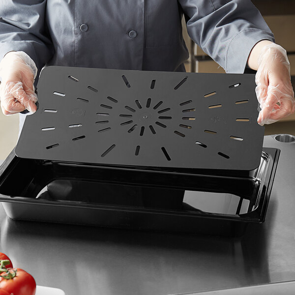 A person holding a black Vigor food pan drain tray on a counter in a professional kitchen.