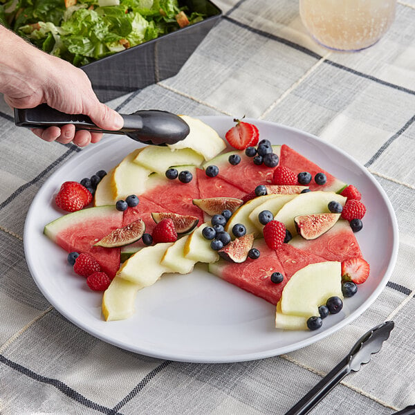A hand using a fork to eat fruit on a white Acopa Lunar melamine plate.