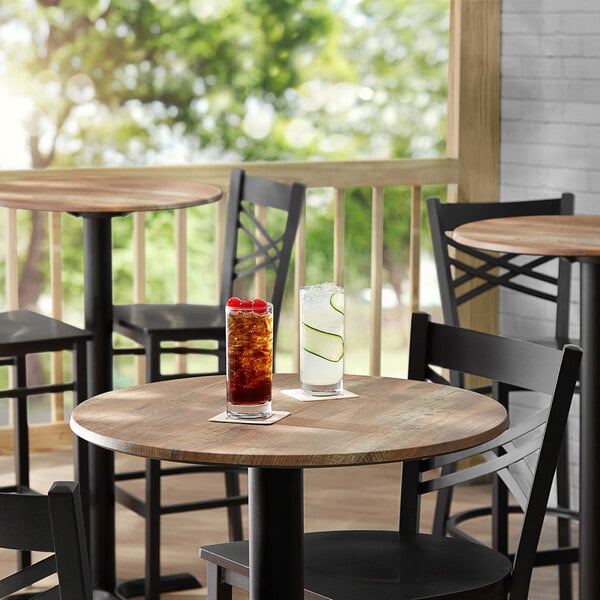 A Lancaster Table & Seating textured Yukon Oak round table with a glass of ice tea and cherries on top.