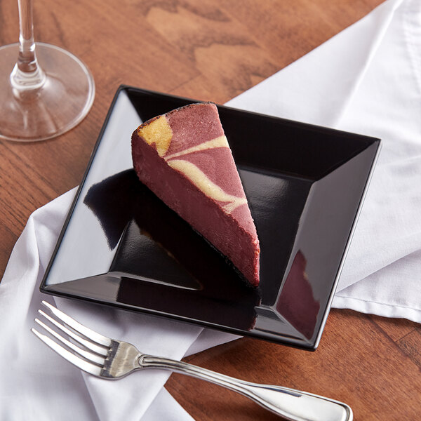 A slice of cake on a black Acopa Rittenhouse square melamine plate with a fork and knife.