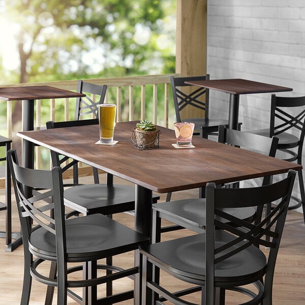 A Lancaster Table & Seating rectangular table with a textured walnut finish, chairs, a drink, and a potted plant on it.