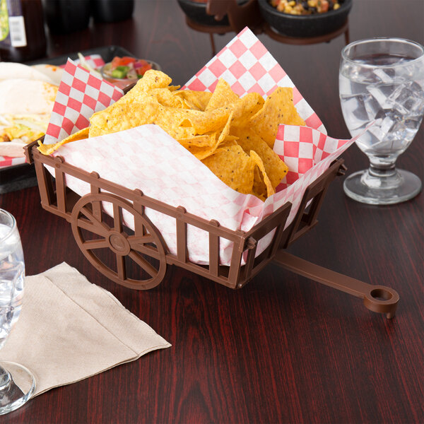 A brown rectangular polypropylene basket on a table with chips and a glass of water.