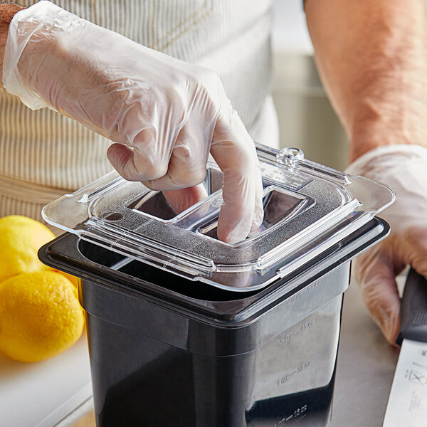 A person wearing gloves using a Vigor clear plastic lid to cover a container of food.