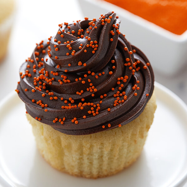 A cupcake with chocolate frosting and orange nonpareils on top.