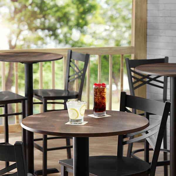 A Lancaster Table & Seating round table with a textured walnut finish and chairs with a drink on it.