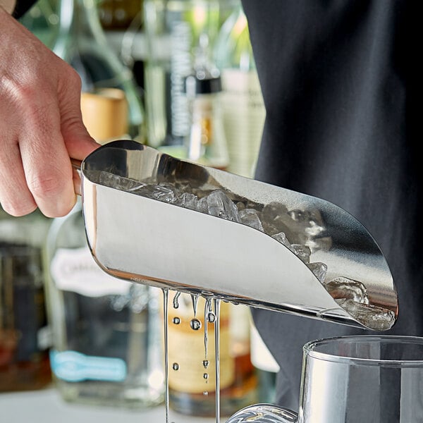 A person using a Tablecraft stainless steel ice scoop to add ice to a glass on a counter.