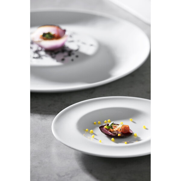 Two Corona by GET Enterprises bright white porcelain plates with food on a table.