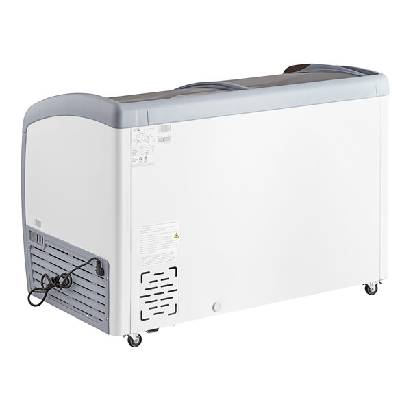 A large, white curved top display ice cream freezer with a gray lid and caster wheels.