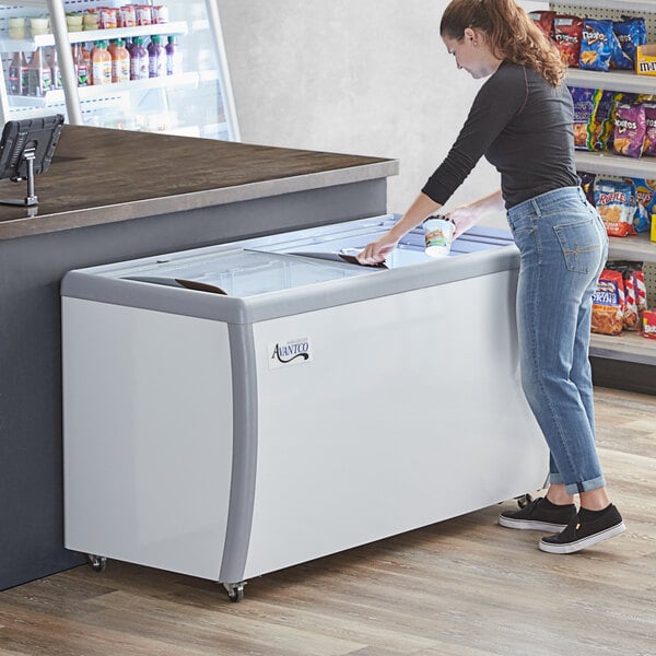 An Avantco flat top glass display freezer on a deli counter with a woman opening the lid.