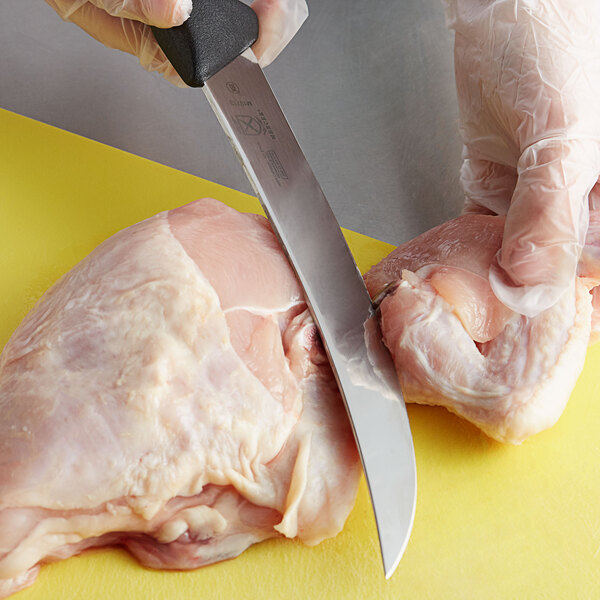 A person using a Mercer Culinary breaking knife to cut a chicken on a counter.