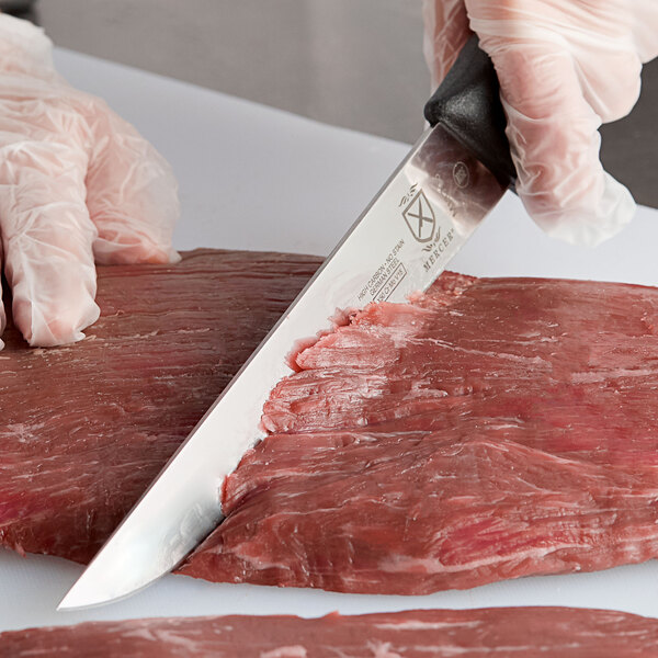 A person using a Mercer Butcher knife to cut meat.
