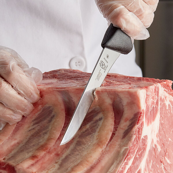 A person using a Mercer Culinary stiff boning knife to cut meat on a counter.