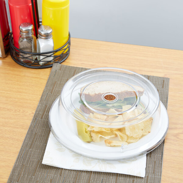 A Carlisle clear polycarbonate plate cover on a table with a sandwich and chips.