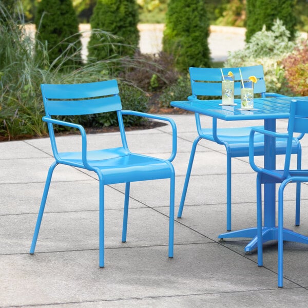 A blue Lancaster Table & Seating outdoor arm chair at a table with a drink on a patio.