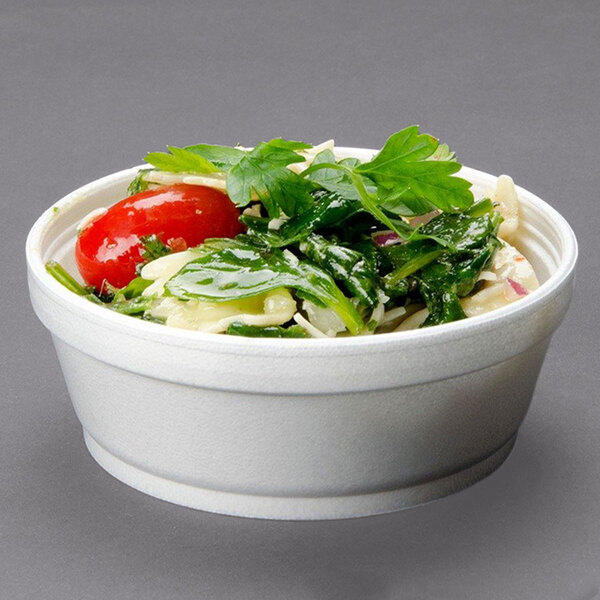 A Dart white foam bowl filled with salad, tomatoes, and spinach.