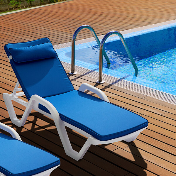 A blue Lancaster Table & Seating chaise cushion on a deck chair next to a pool.