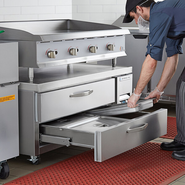A man opening a drawer in a Beverage-Air refrigerated chef base on a counter in a professional kitchen.