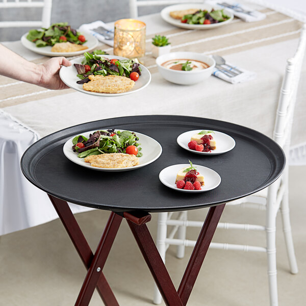 A person holding a black oval non-skid serving tray with food on it.