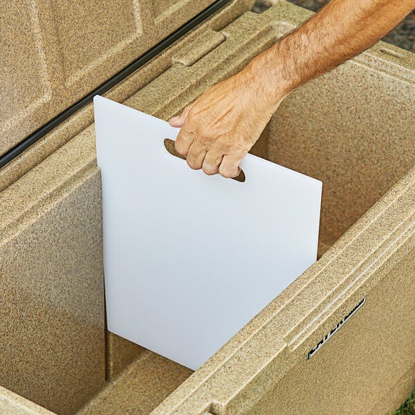 A hand using a white CaterGator plastic divider/cutting board in a cooler.