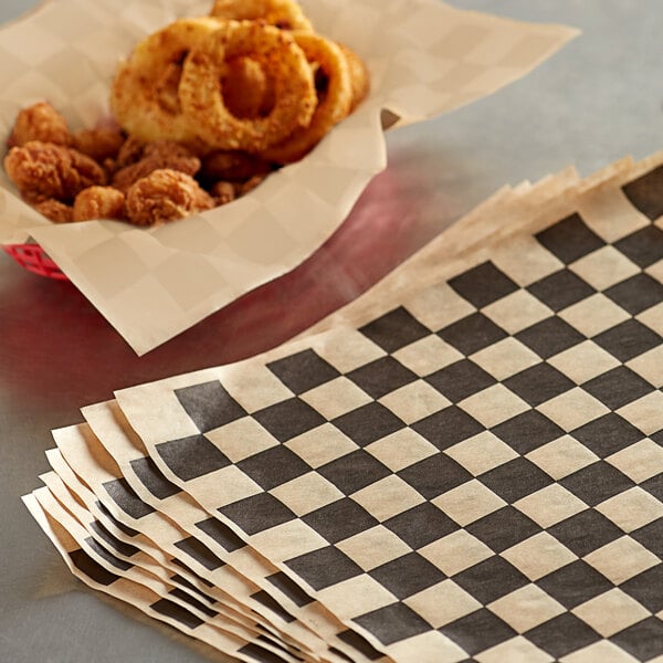 A basket of fried onion rings next to a stack of black checkered deli wrap paper.