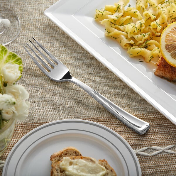 A Visions silver plastic fork on a table next to a plate of pasta with lemon slices.