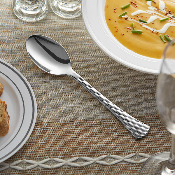 A Visions silver plastic spoon next to a bowl of soup on a table.