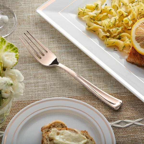 A Visions rose gold plastic fork next to a plate of pasta with lemon slices.