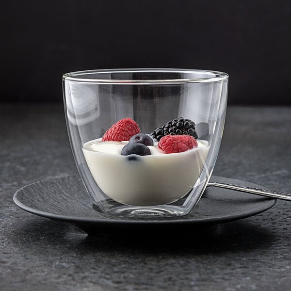 A Villeroy & Boch double wall glass cup of yogurt and berries on a saucer.