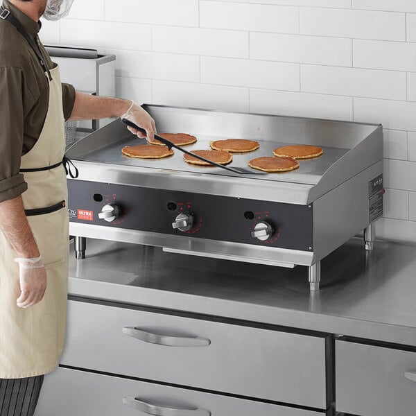 A man wearing a brown shirt cooking pancakes on a Cooking Performance Group countertop griddle.