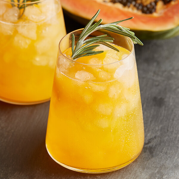 A glass of orange liquid with ice and a sprig of rosemary.