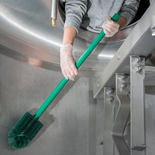A person in gloves cleaning a stainless steel sink with a Carlisle green brush with a green handle.