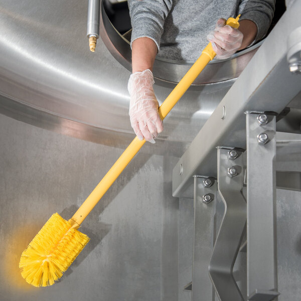 A person in gloves holding a yellow Carlisle Sparta multi-purpose brush.
