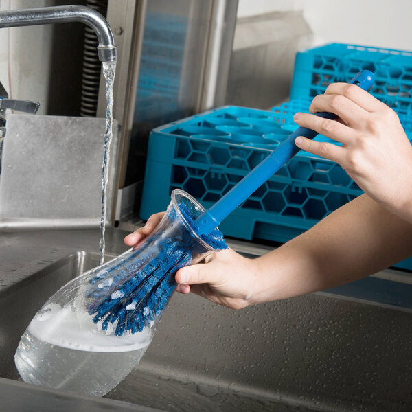 A person using a Carlisle blue bottle cleaning brush to clean a glass container.