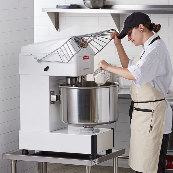 A woman in a white apron using an Estella spiral dough mixer to mix dough.