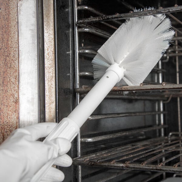 A hand in white gloves using a Carlisle white multi-purpose brush to clean.
