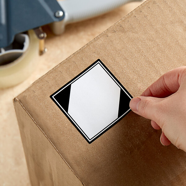A hand using a white Lavex label to put on a cardboard box.
