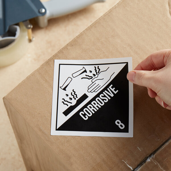 A hand using a Lavex corrosive gloss paper label to apply a sticker to a box.