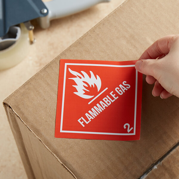 A hand uses a Lavex Flammable Gas label to put on a box.
