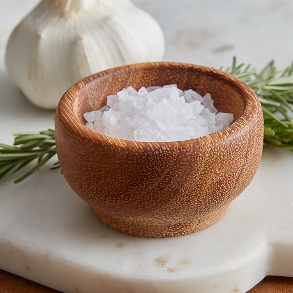 A Fox Run acacia wood condiment cup filled with salt next to garlic.