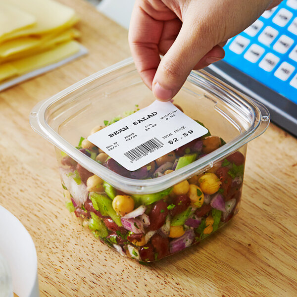 A hand placing a Globe E11 white label on a plastic container of food.