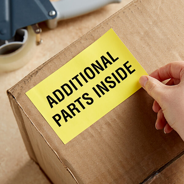 A hand holding a Lavex matte paper label on a cardboard box with the words "additional parts inside"