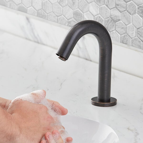 A person washing their hands under a Waterloo bronze hands-free sensor faucet.