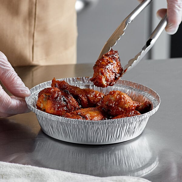 A gloved hand using tongs to serve chicken from a Choice foil take-out pan.
