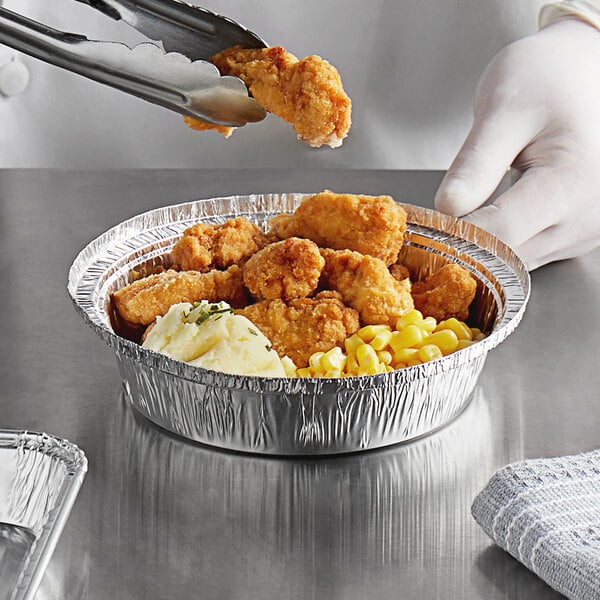 A person holding a Choice heavy weight foil take-out container of fried chicken and mashed potatoes.