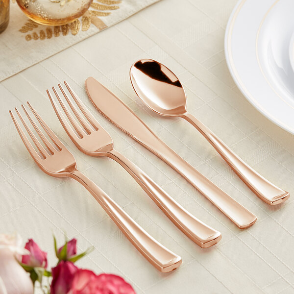 A Visions rose gold plastic cutlery set on a table with a spoon and knife.
