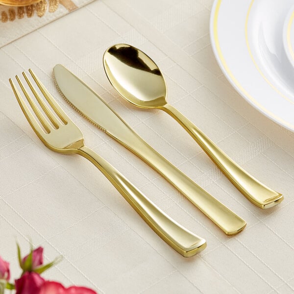 A Visions Classic gold plastic spoon, fork, and knife set on a white tablecloth.