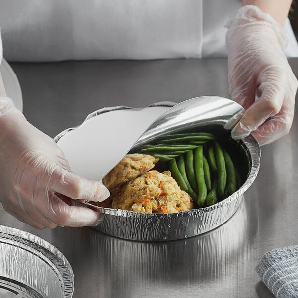 A person in gloves putting green beans and chicken in a Choice foil-laminated board lid.